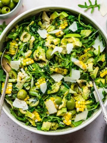 close up overhead view of corn avocado arugula salad with basil dressing in large bowl.