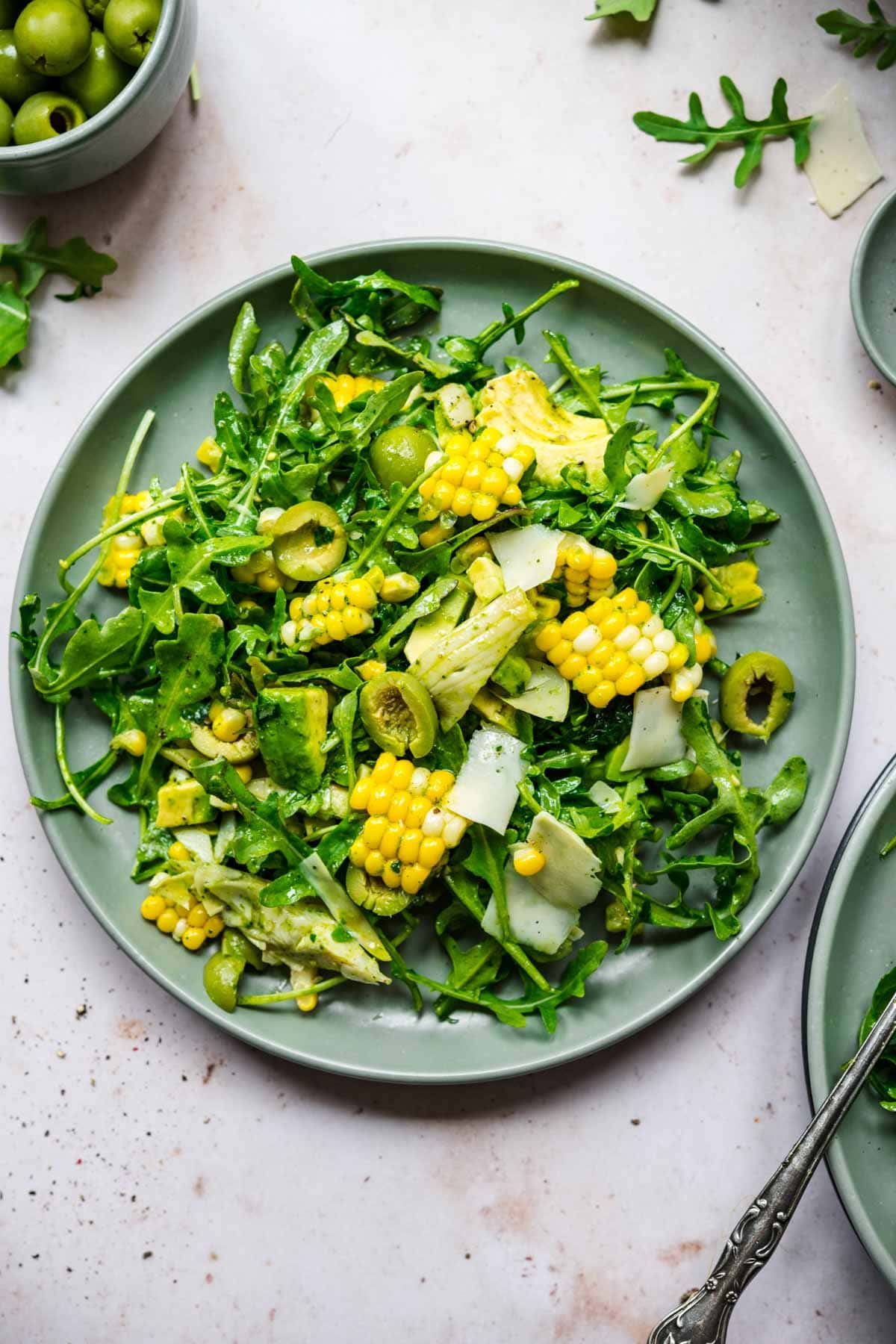 close up overhead view of corn avocado arugula salad with basil dressing on a green plate.