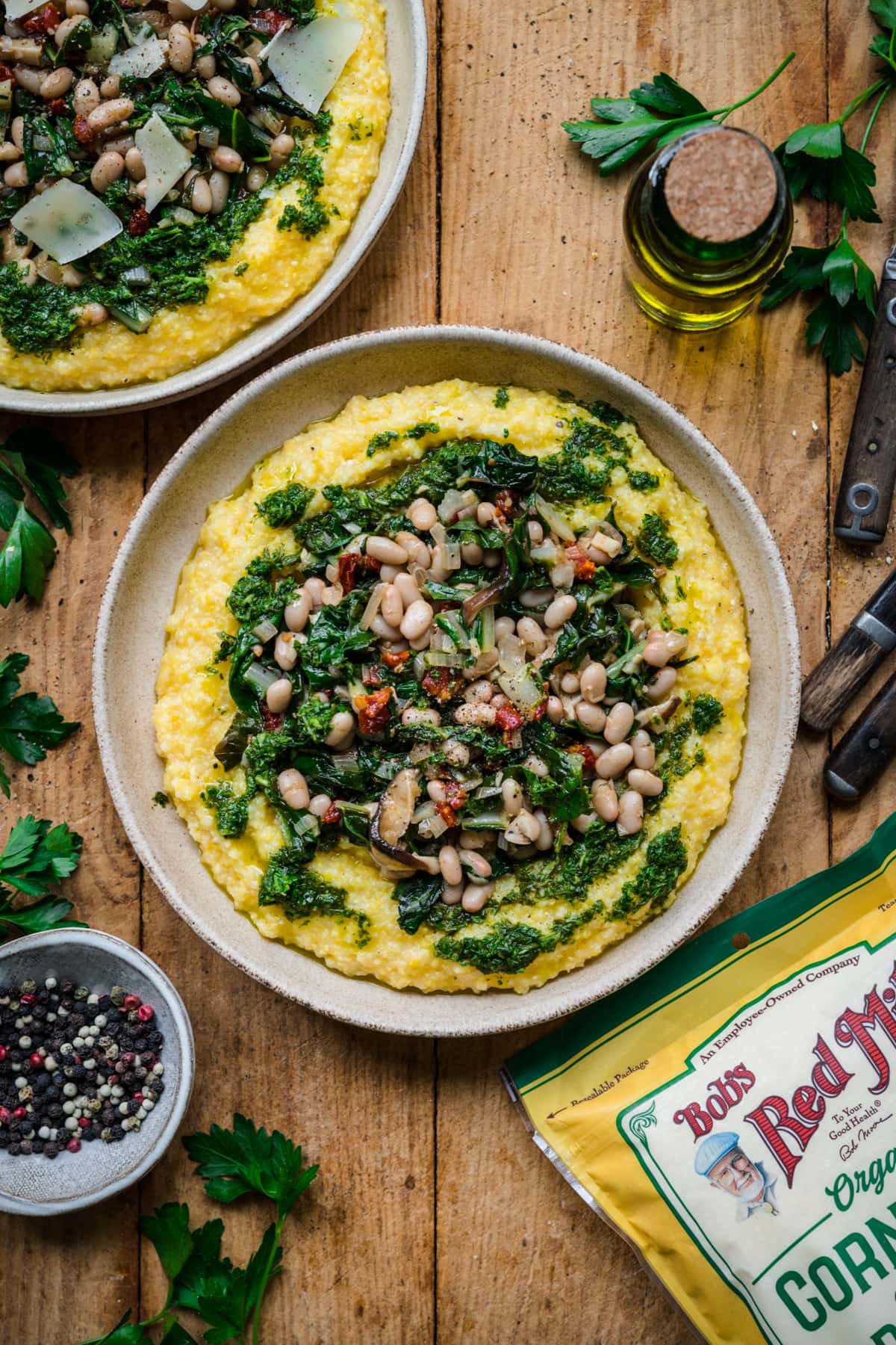 overhead view of vegan polenta topped with white beans, sautéed vegetables and herb oil. 