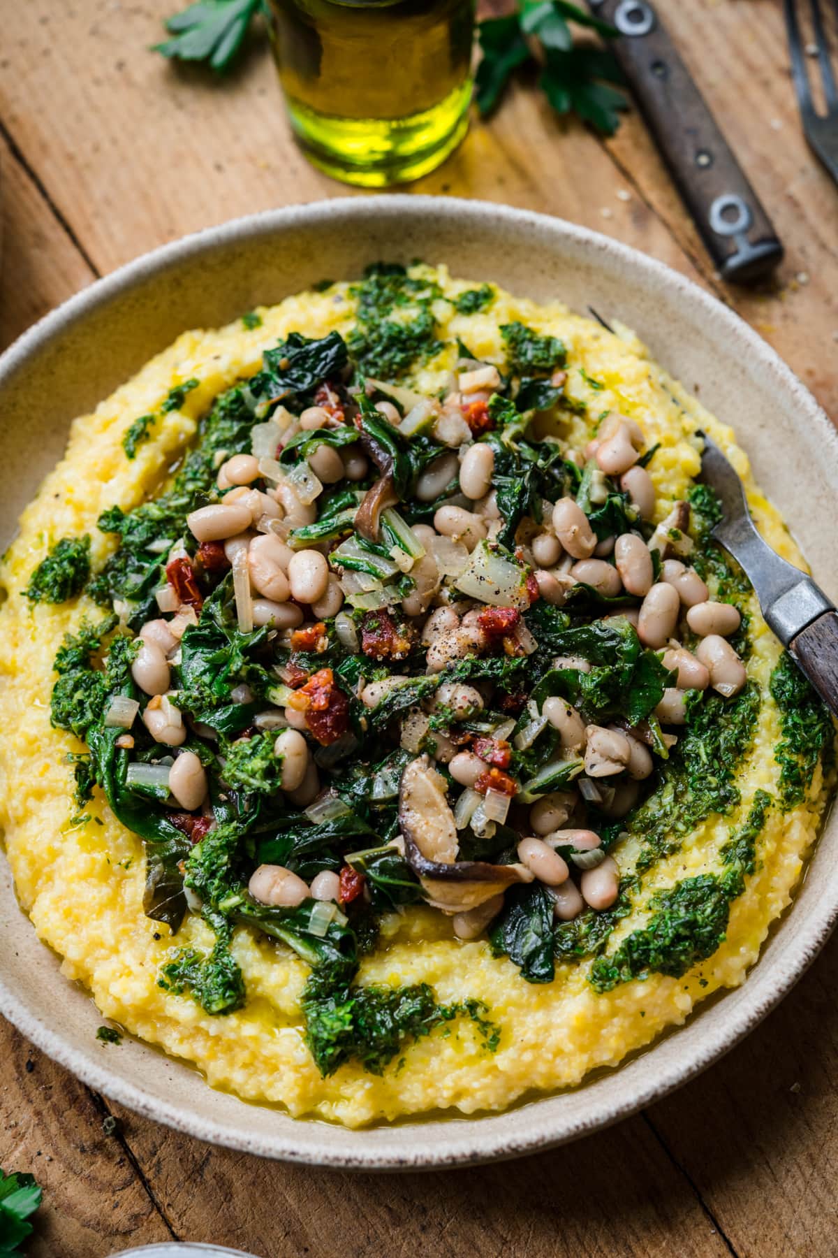 close up view of vegan polenta topped with white beans, sautéed vegetables and herb oil. 