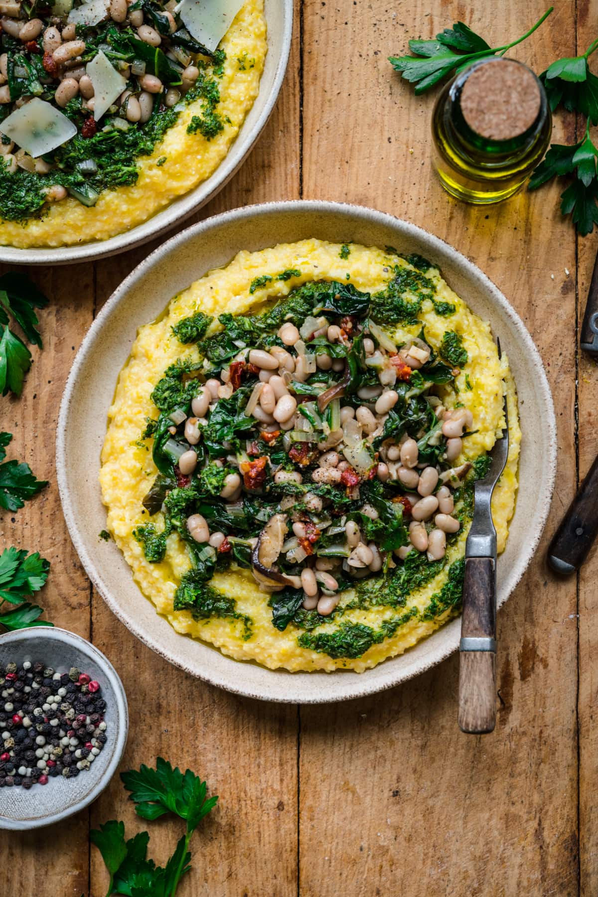 overhead view of vegan polenta topped with white beans, sautéed vegetables and herb oil. 