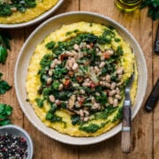 overhead view of vegan polenta topped with white beans, sautéed vegetables and herb oil.