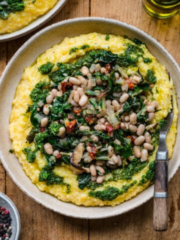 overhead view of vegan polenta topped with white beans, sautéed vegetables and herb oil.