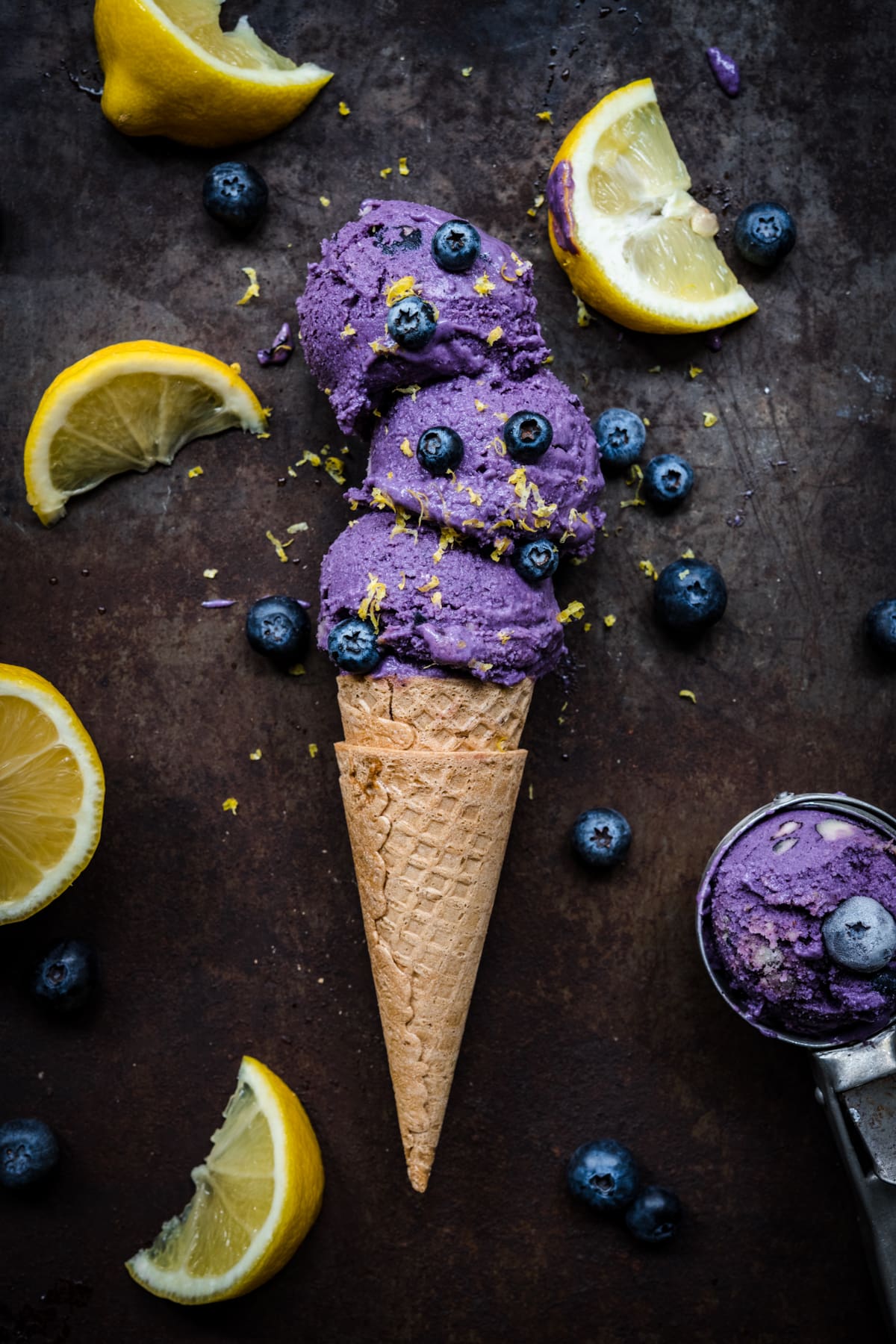 overhead view of vegan lemon blueberry ice cream in an ice cream cone with blueberries and lemon zest.