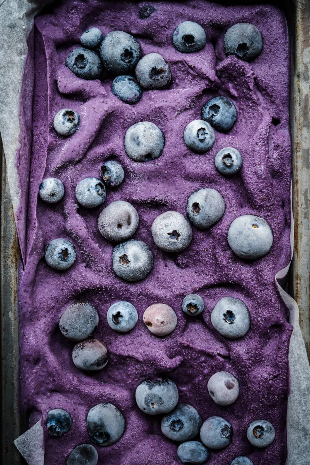 close up view of vegan lemon blueberry ice cream in a loaf pan with frozen blueberries on top.