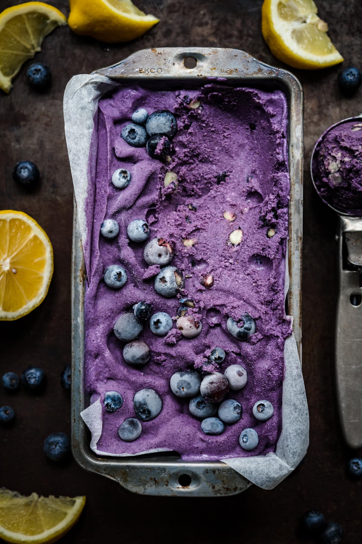 overhead view of vegan lemon blueberry ice cream in a loaf pan with frozen blueberries on top.