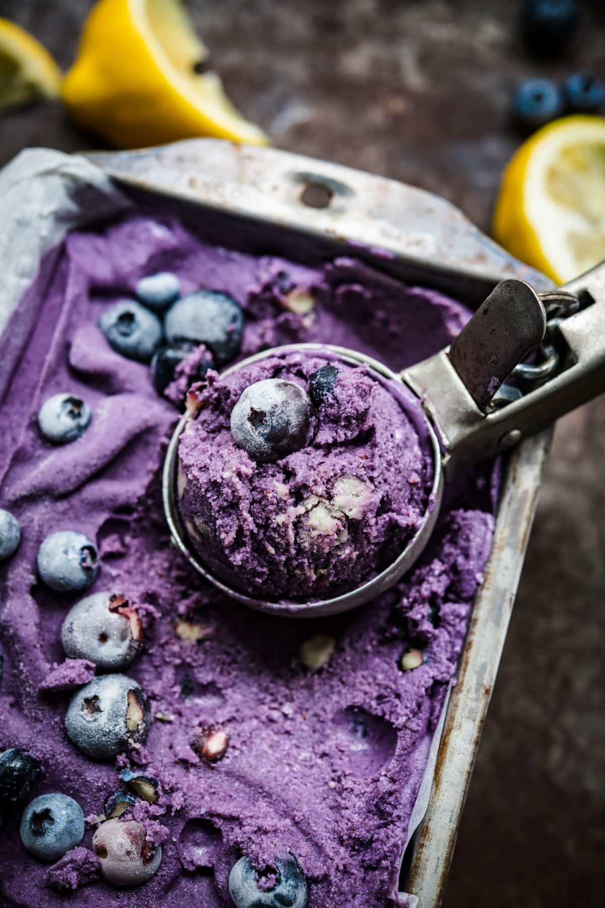 close up view of vegan lemon blueberry ice cream in a loaf pan ice cream in scoop. 