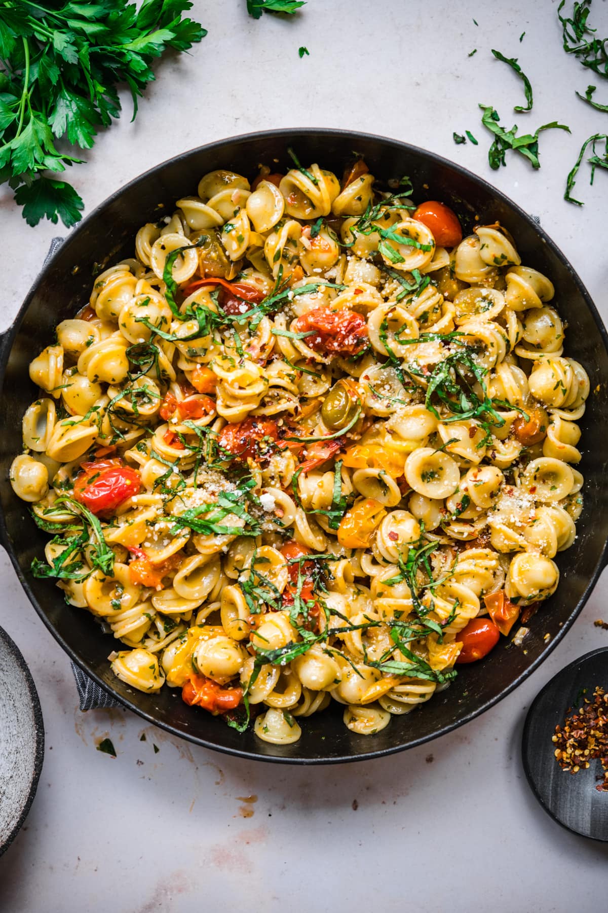 overhead view of burst cherry tomato pasta with fresh basil and red pepper flakes in skillet.