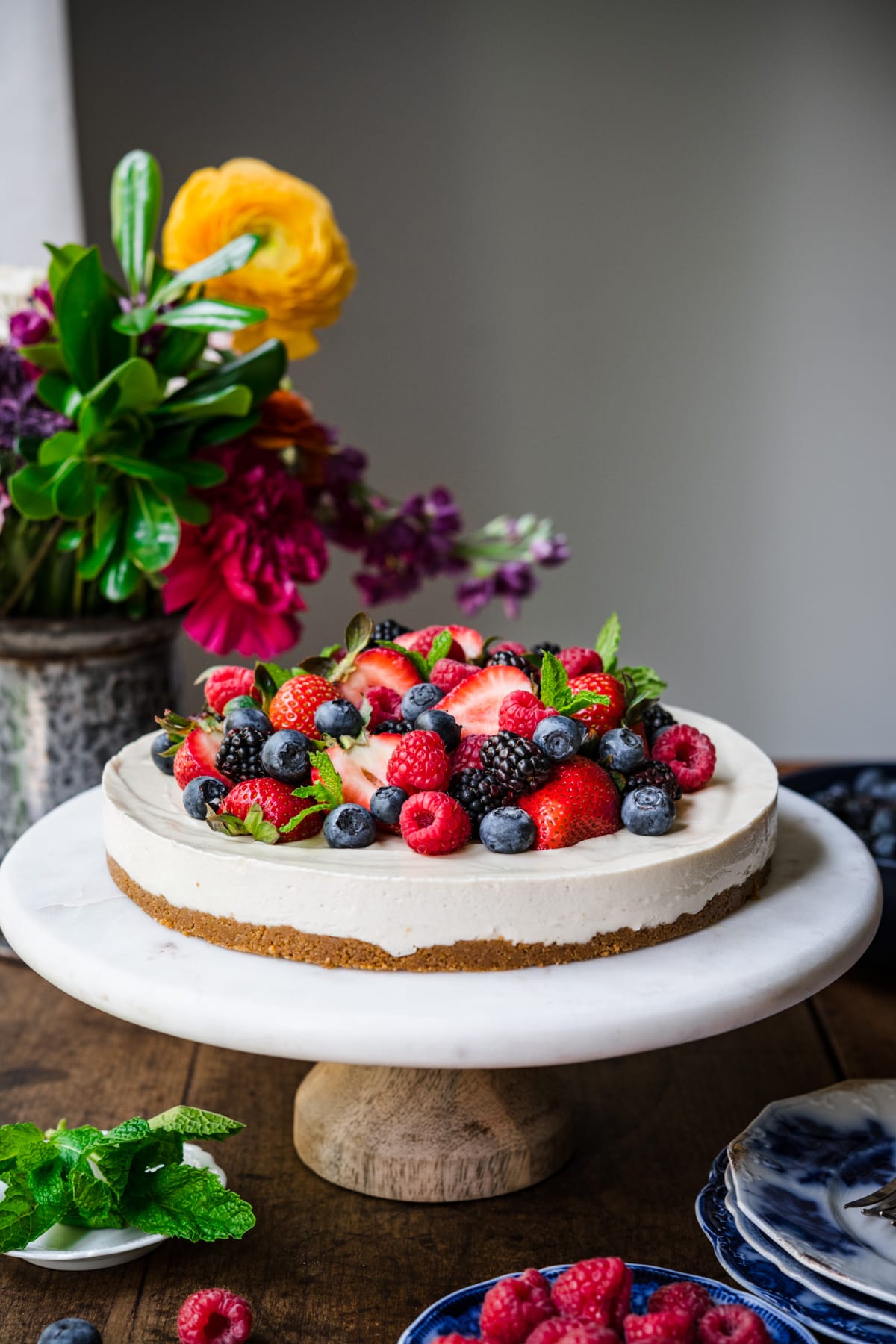 side view of no bake vegan cheesecake topped with fresh berries on a marble cake stand. 