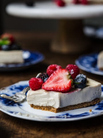 close up side view of slice of vegan no bake cheesecake on a blue china plate with fresh berries.
