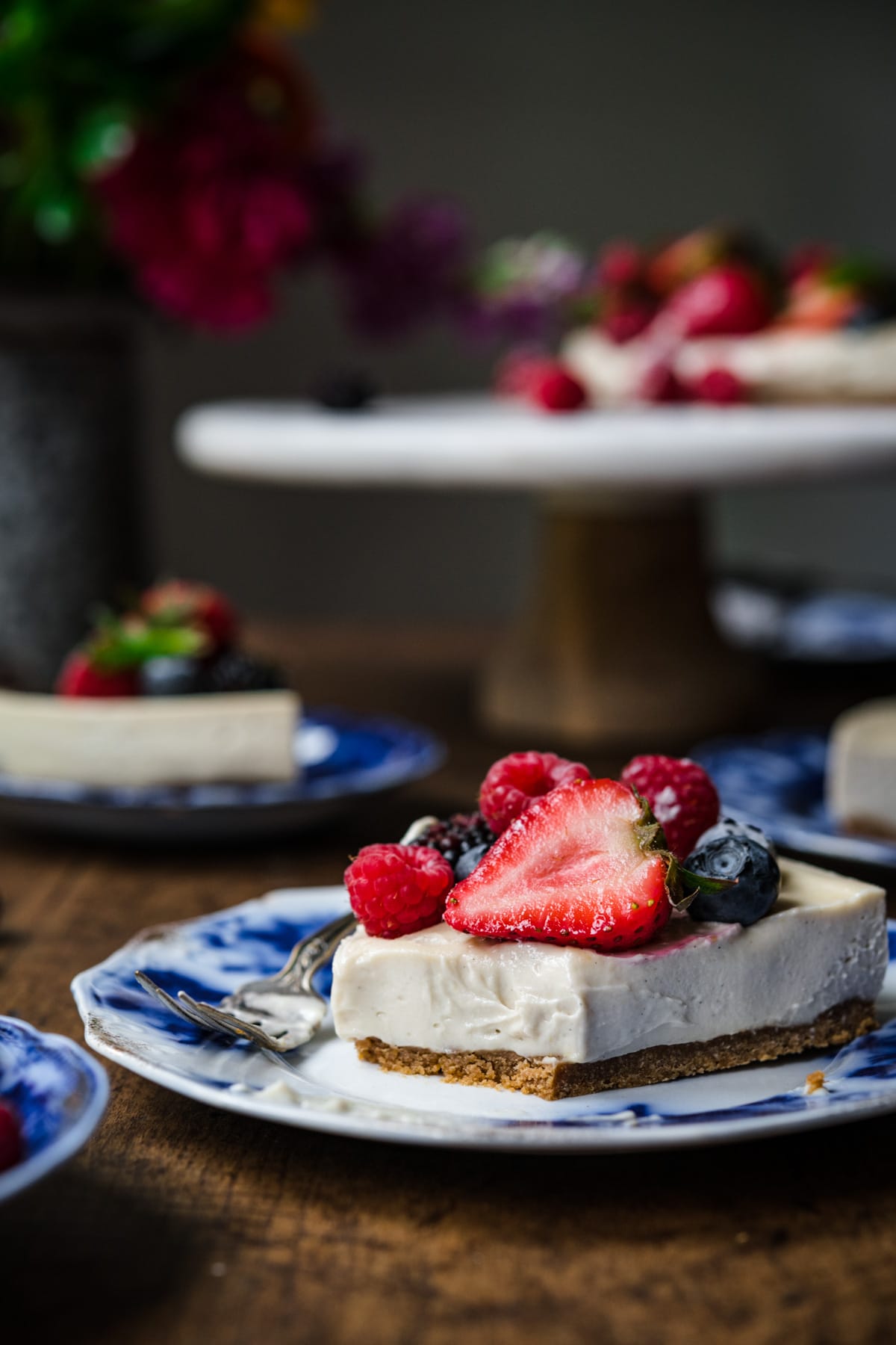 close up side view of slice of vegan no bake cheesecake on a blue china plate with fresh berries. 