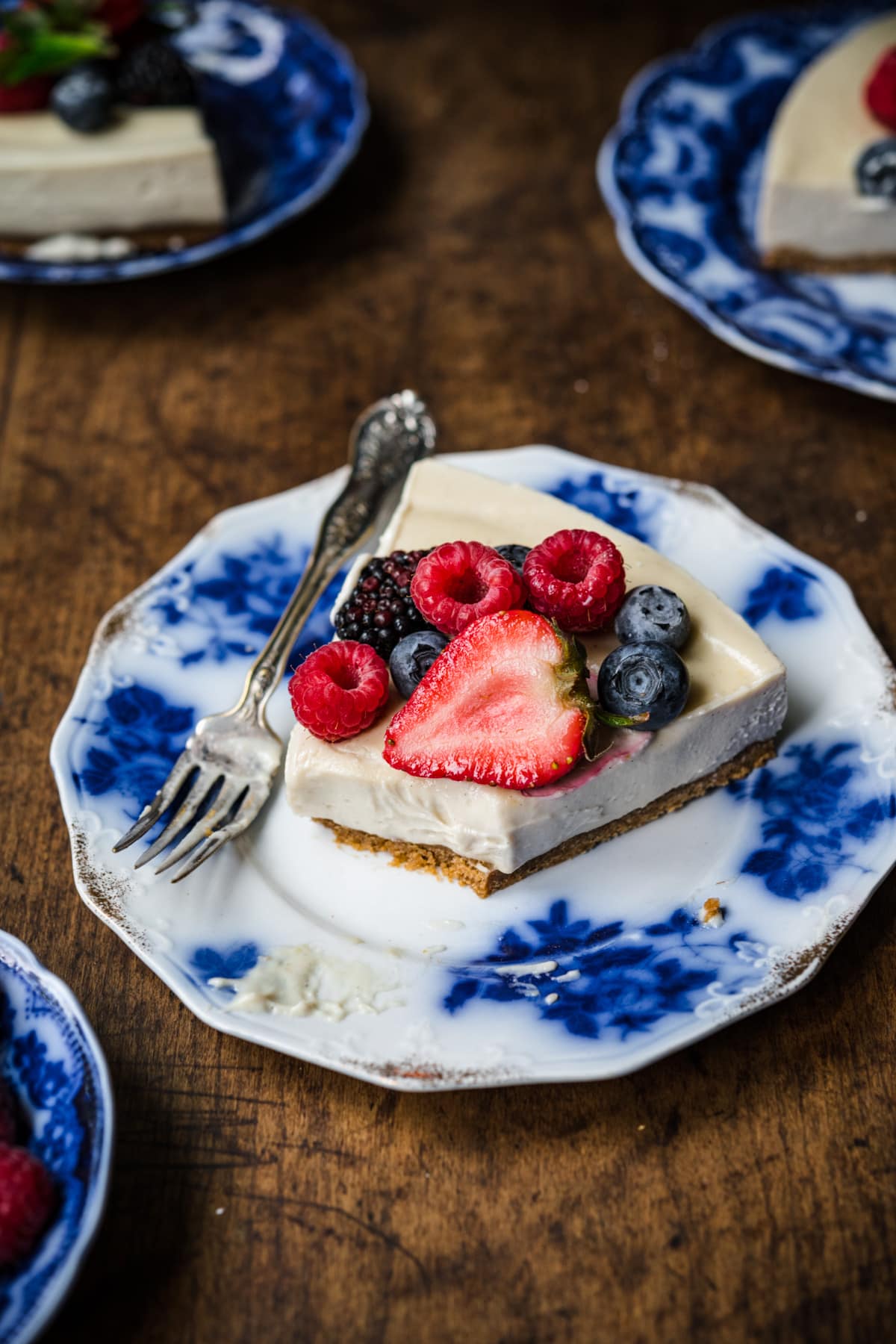 close up side view of slice of vegan no bake cheesecake on a blue china plate with fresh berries. 