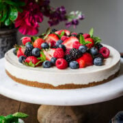 side view of no bake vegan cheesecake topped with fresh berries on a marble cake stand.