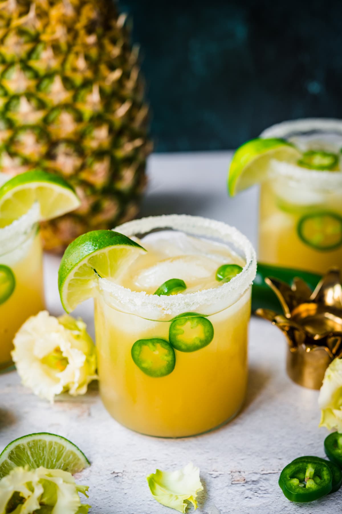 side view of pineapple jalapeño margarita in glass rimmed with salt with a fresh pineapple in background. 