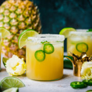 side view of pineapple jalapeño margarita in glass rimmed with salt with a fresh pineapple in background.