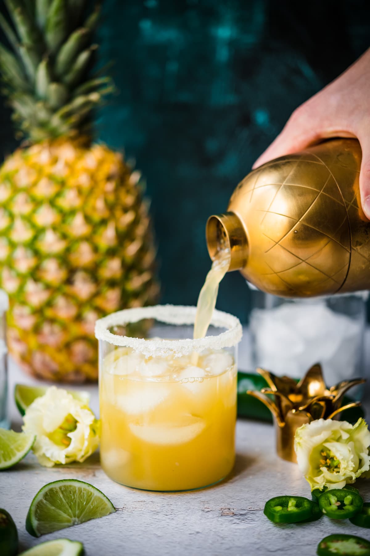 pouring pineapple jalapeño margarita from cocktail shaker into glass with salt rim and ice. 