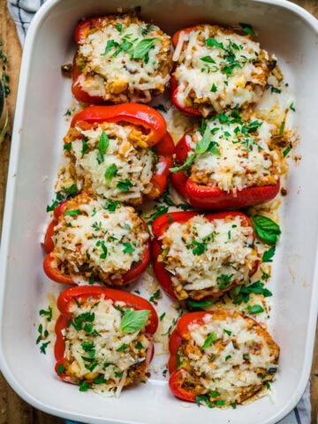 overhead view of vegan stuffed red peppers with cheese on top in baking dish.
