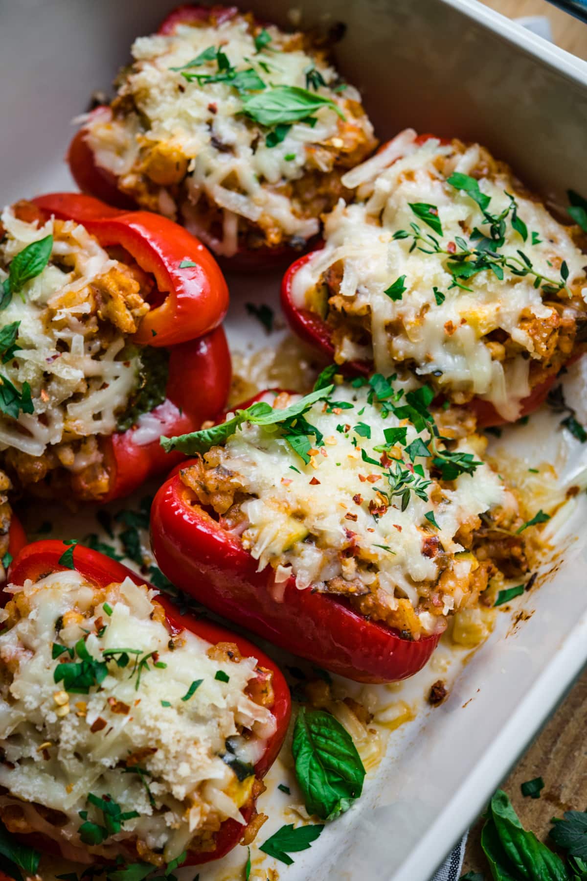 close up view of vegan stuffed red peppers with cheese on top in baking dish. 