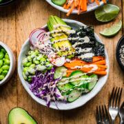 overhead view of vegan sushi bowl with avocado, radishes, cucumber, edamame and miso tahini dressing.