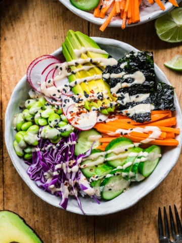 overhead view of vegan sushi bowl with avocado, radishes, cucumber, edamame and miso tahini dressing.