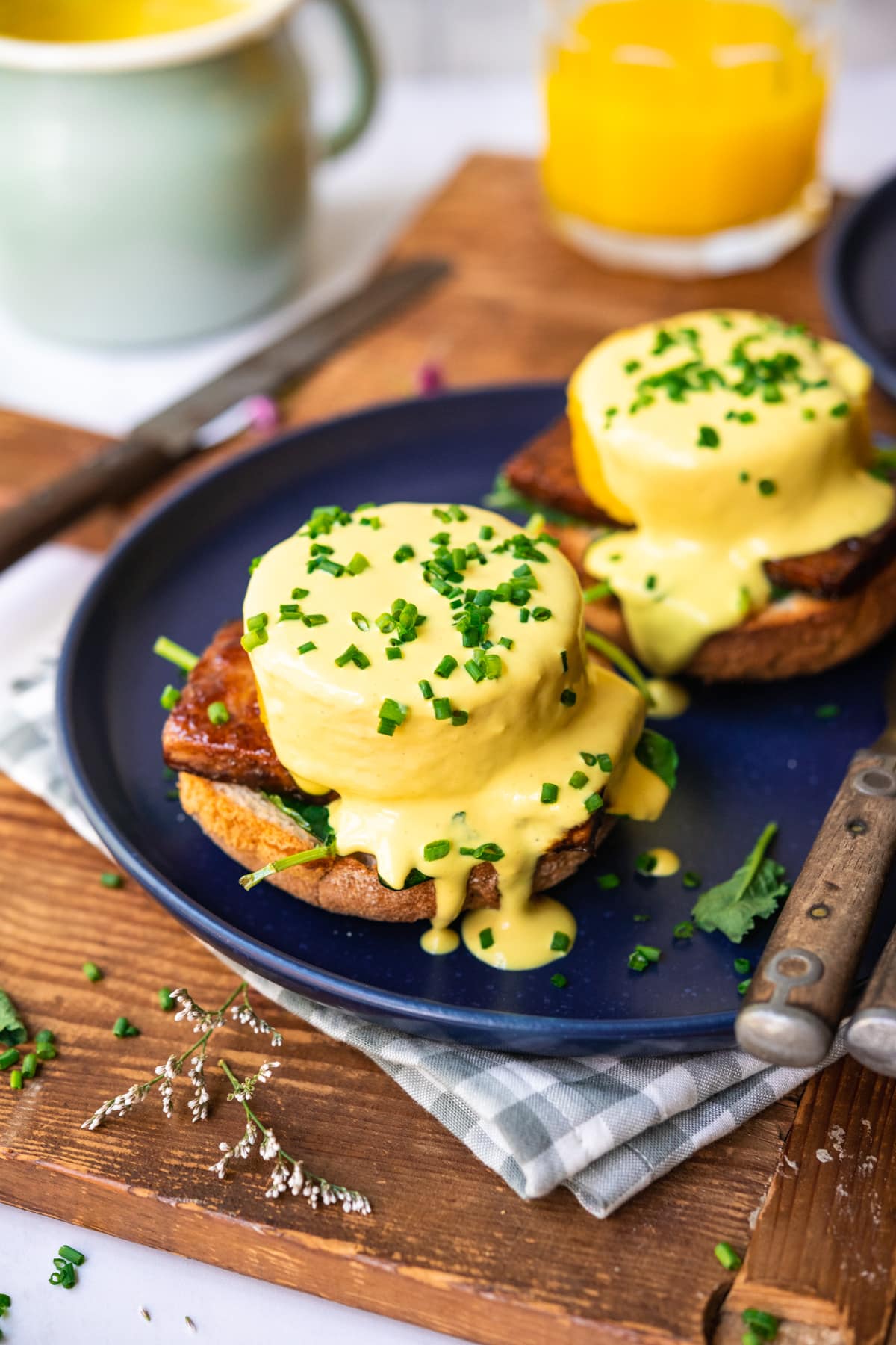 side view of vegan eggs benedict on a blue plate with hollandaise sauce and chives. 