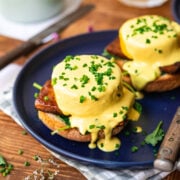 side view of vegan eggs benedict on a blue plate with hollandaise sauce and chives.