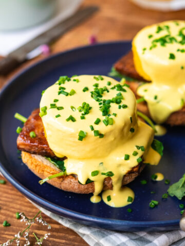 side view of vegan eggs benedict on a blue plate with hollandaise sauce and chives.