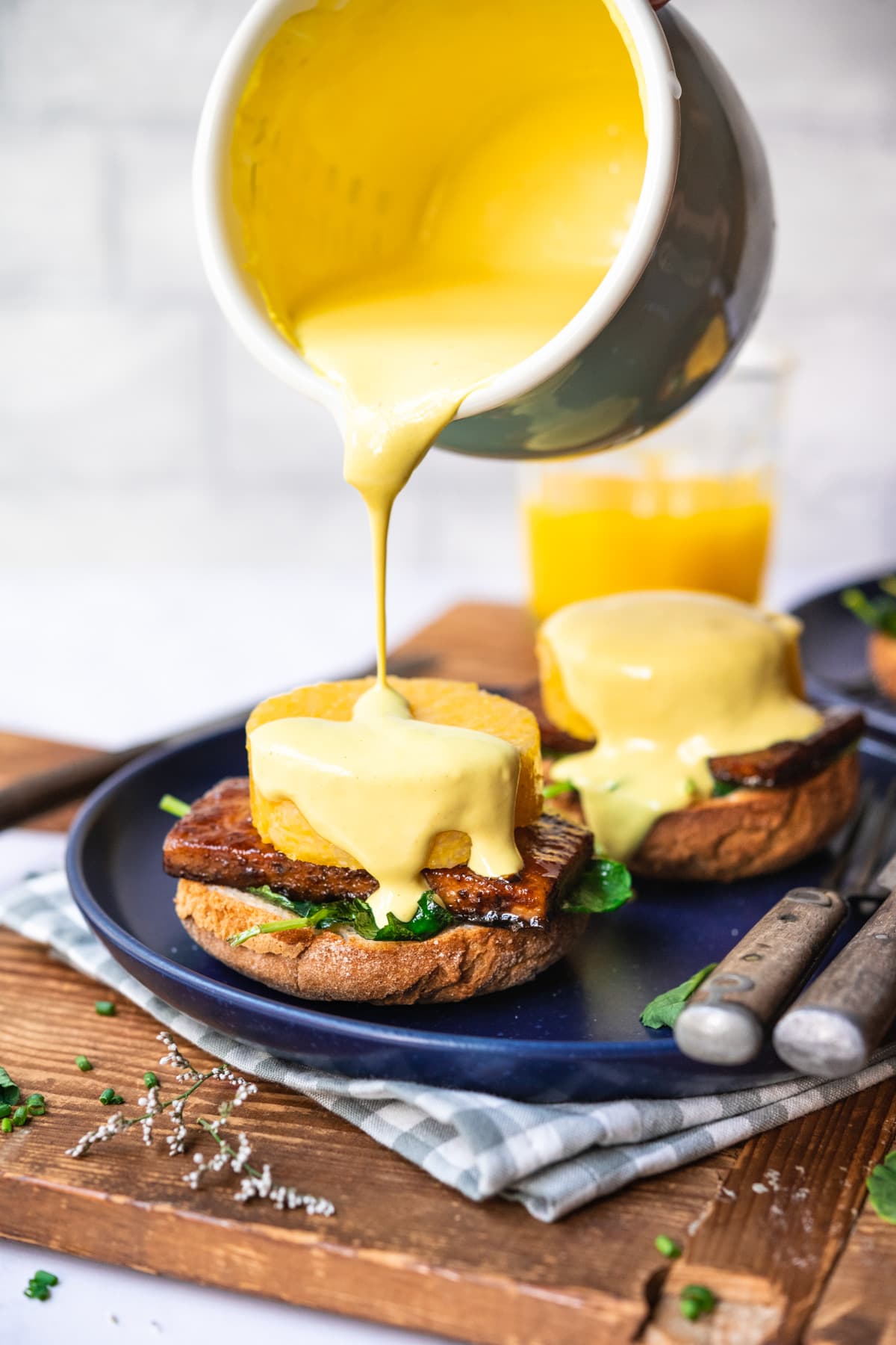 pouring vegan hollandaise sauce onto polenta eggs benedict on blue plate. 