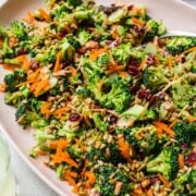 close up side view of vegan broccoli salad with cranberries and sunflower seeds on light pink platter.