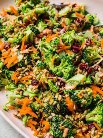 close up side view of vegan broccoli salad with cranberries and sunflower seeds on light pink platter.