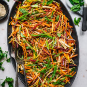 overhead view of shaved rainbow carrot salad with miso sesame dressing on large black platter.