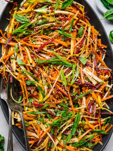 overhead view of shaved rainbow carrot salad with miso sesame dressing on large black platter.