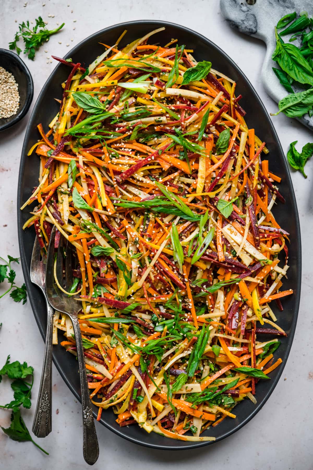 overhead view of shaved rainbow carrot salad with miso sesame dressing on large black platter. 