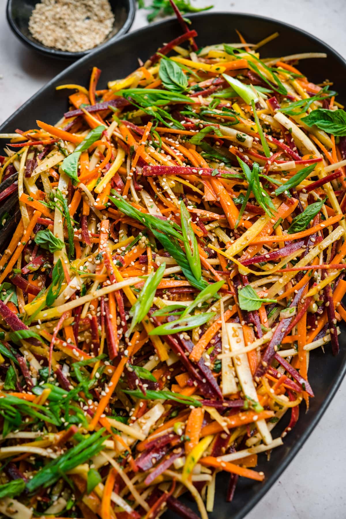 close up view of shaved rainbow carrot salad with miso sesame dressing on large black platter. 