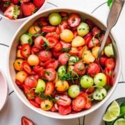 close up overhead view of melon ball salad with strawberries and mint in white bowl.