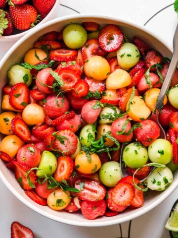 close up overhead view of melon ball salad with strawberries and mint in white bowl.