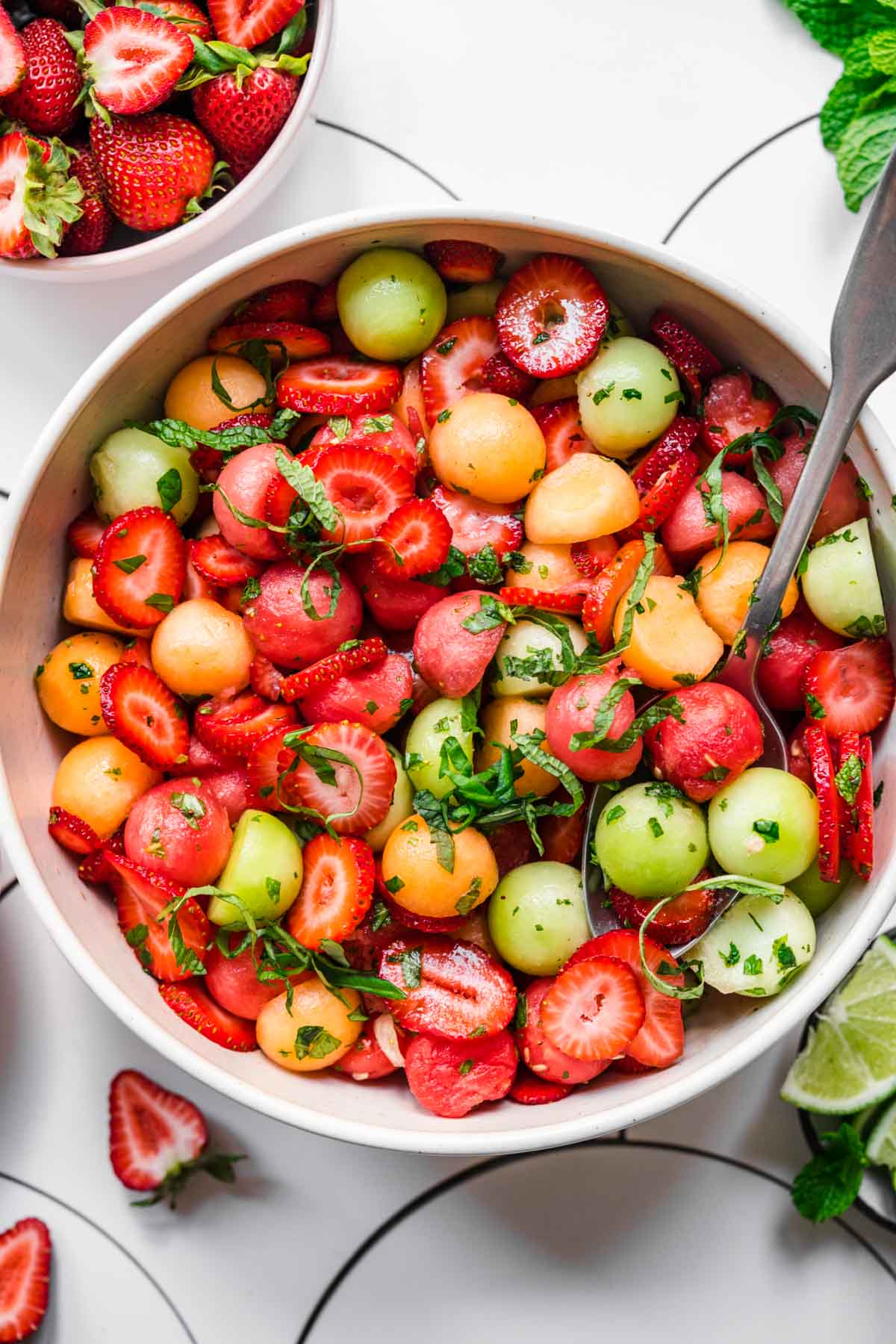 close up overhead view of melon ball salad with strawberries and mint in white bowl. 