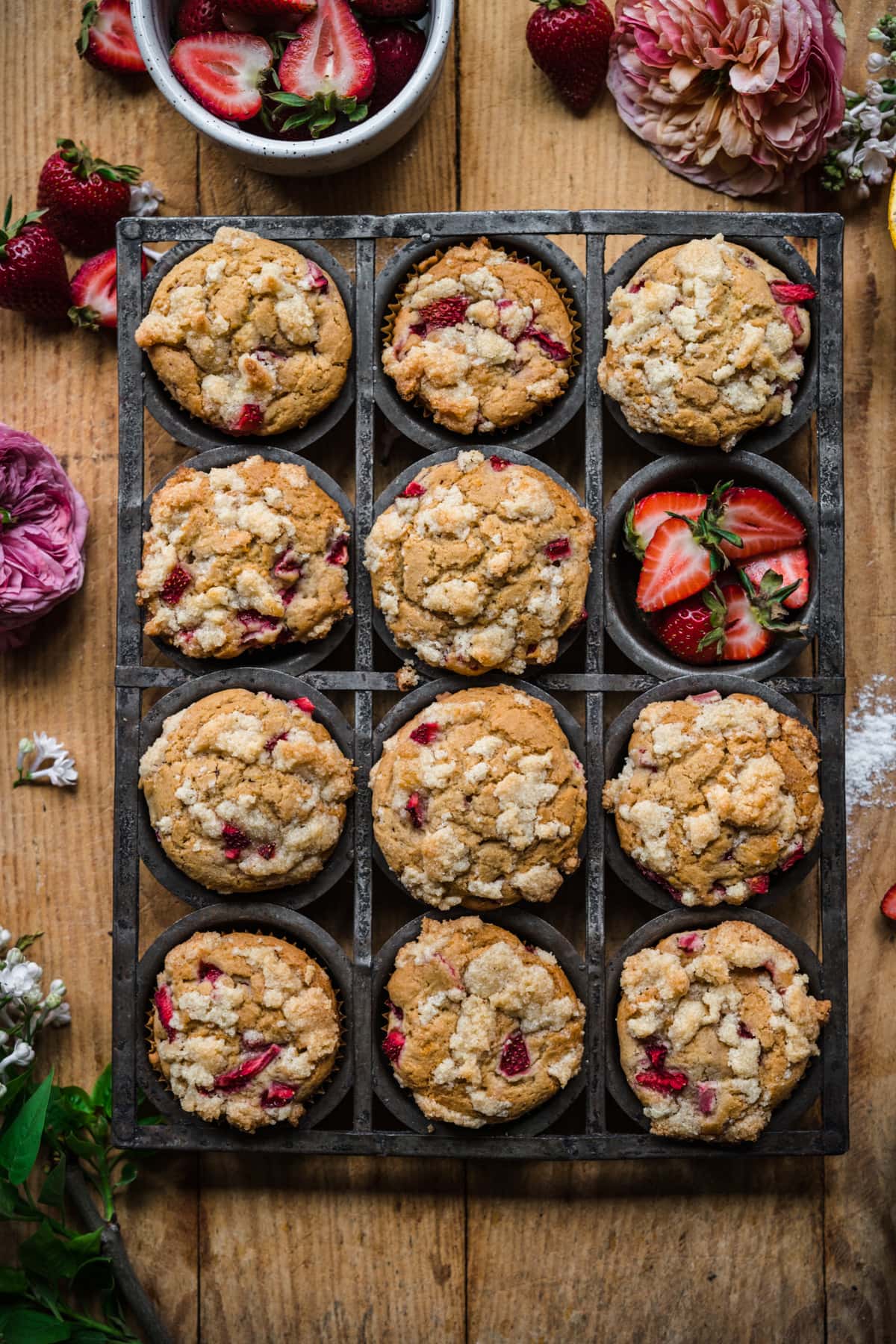 overhead view of vegan strawberry muffins with almond streusel in antique muffin tin on wood surface. 