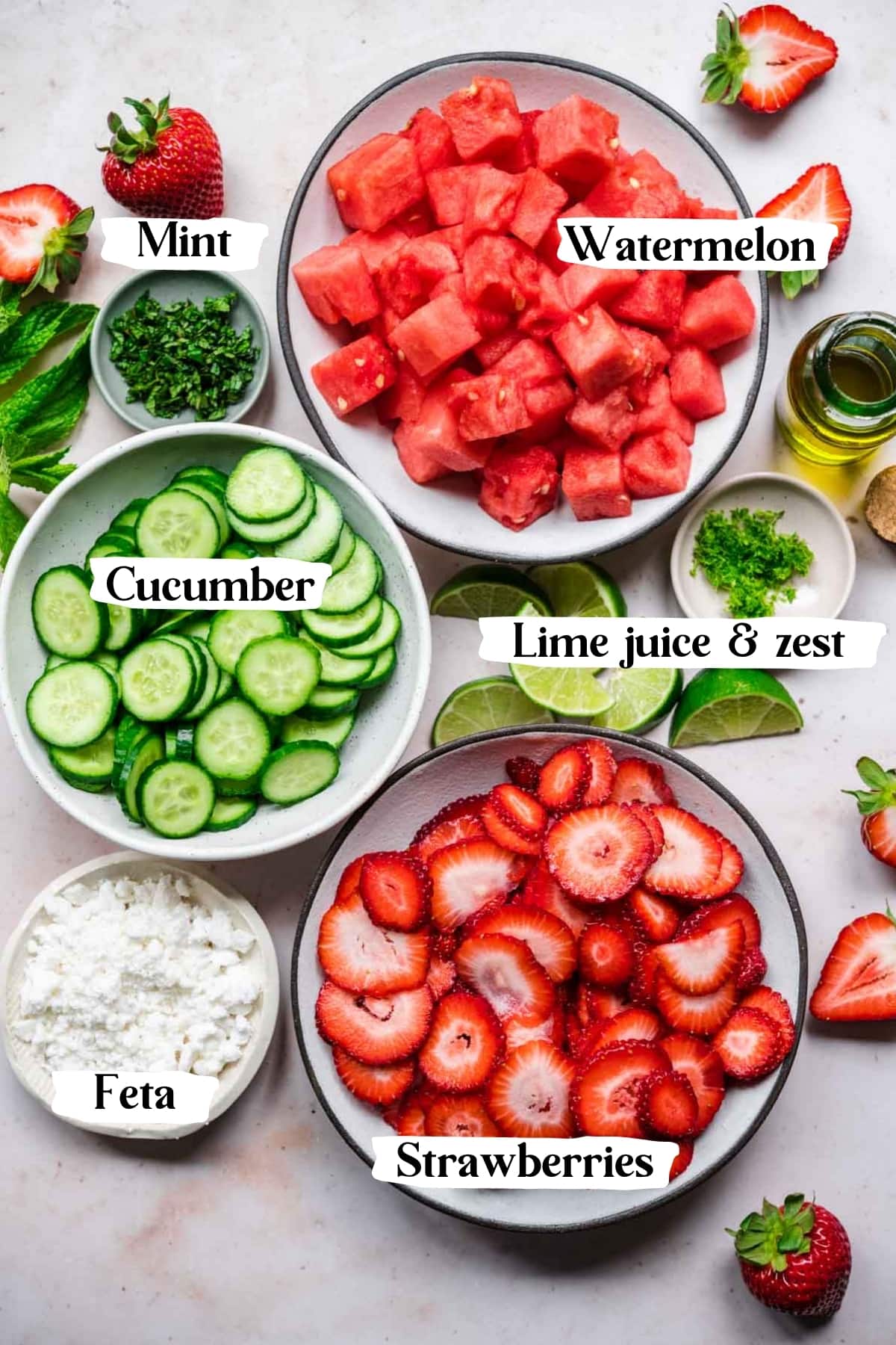 overhead view of ingredients for watermelon cucumber strawberry salad in prep bowls. 