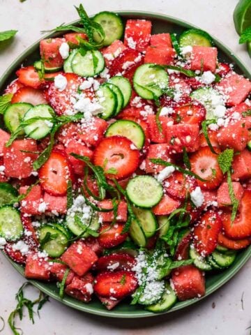close up overhead view of watermelon cucumber strawberry salad on a plate with mint and feta.