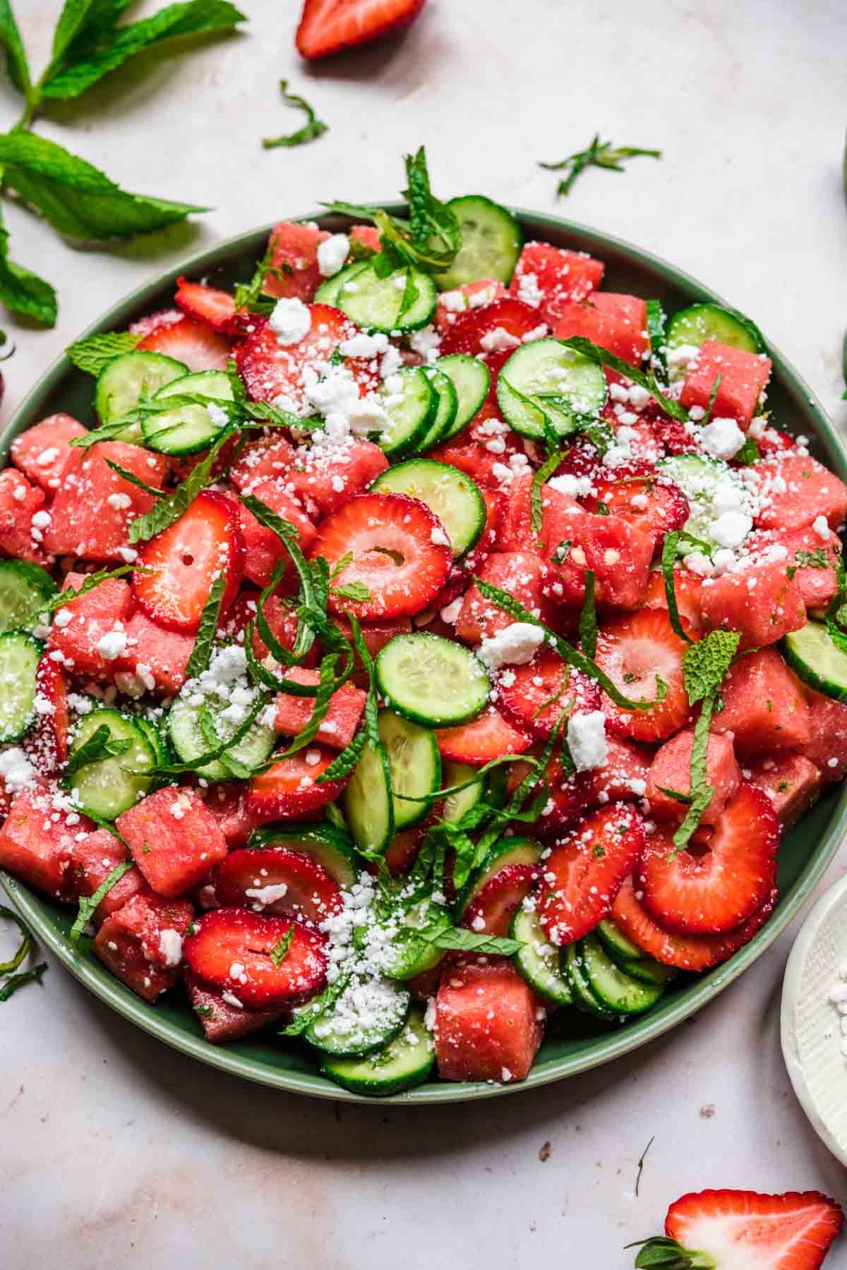 close up view of watermelon cucumber strawberry salad on a plate with mint and feta. 