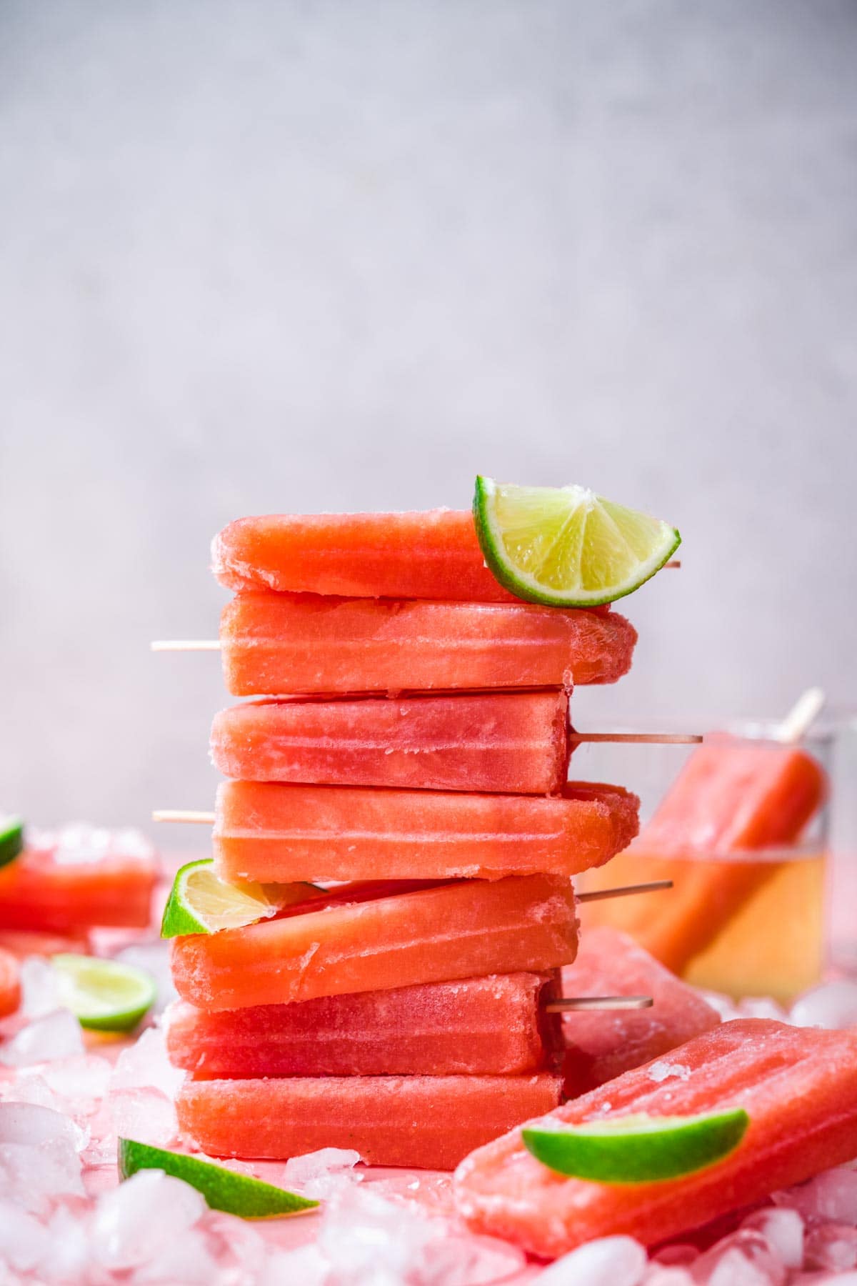 stack of watermelon prosecco popsicles with crushed ice and lime wedges. 