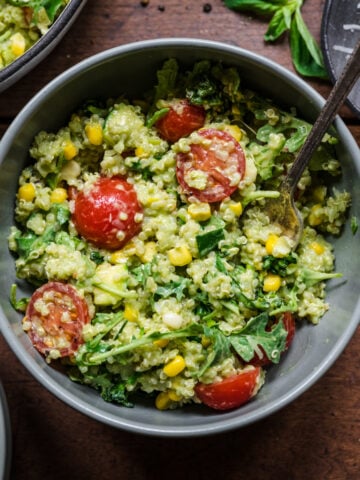 Green goddess salad in a bowl with a spoon. Full of quinoa and cherry tomatoes.