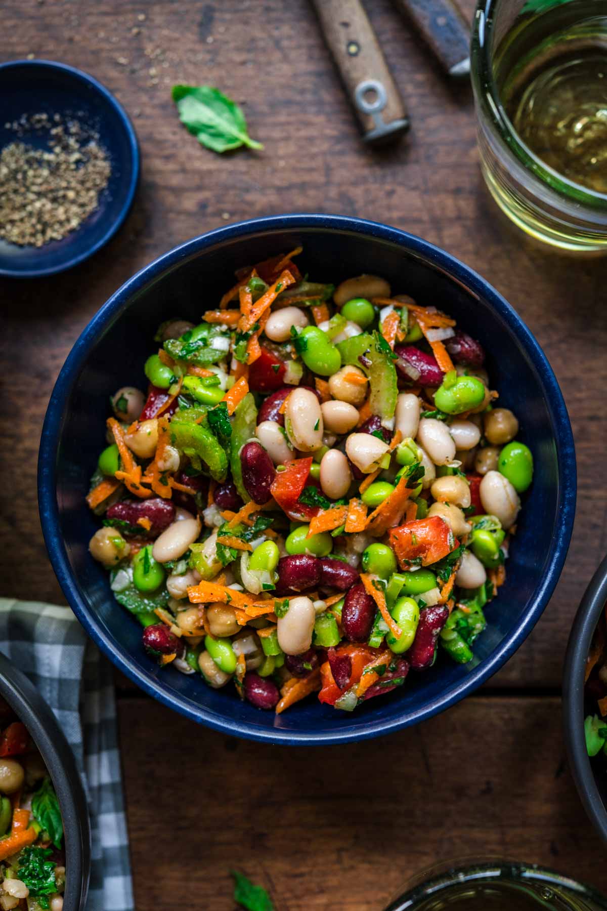 close up view of four bean salad in a blue bowl on wood table. 