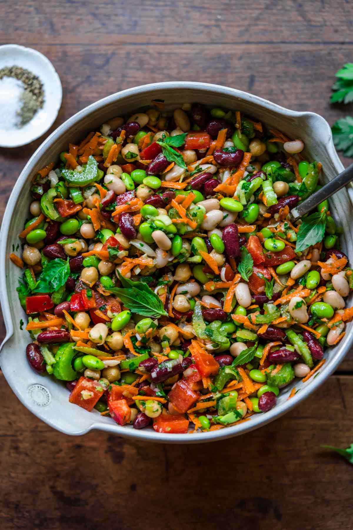 close up view of four bean salad in a large white mixing bowl on wood table. 