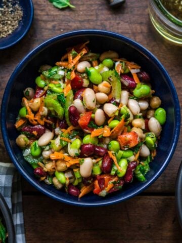 close up view of four bean salad in a blue bowl on wood table.