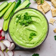 overhead view of herb tofu dip in bowl with fresh vegetables and crackers next to it.