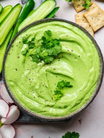 overhead view of herb tofu dip in bowl with fresh vegetables and crackers next to it.