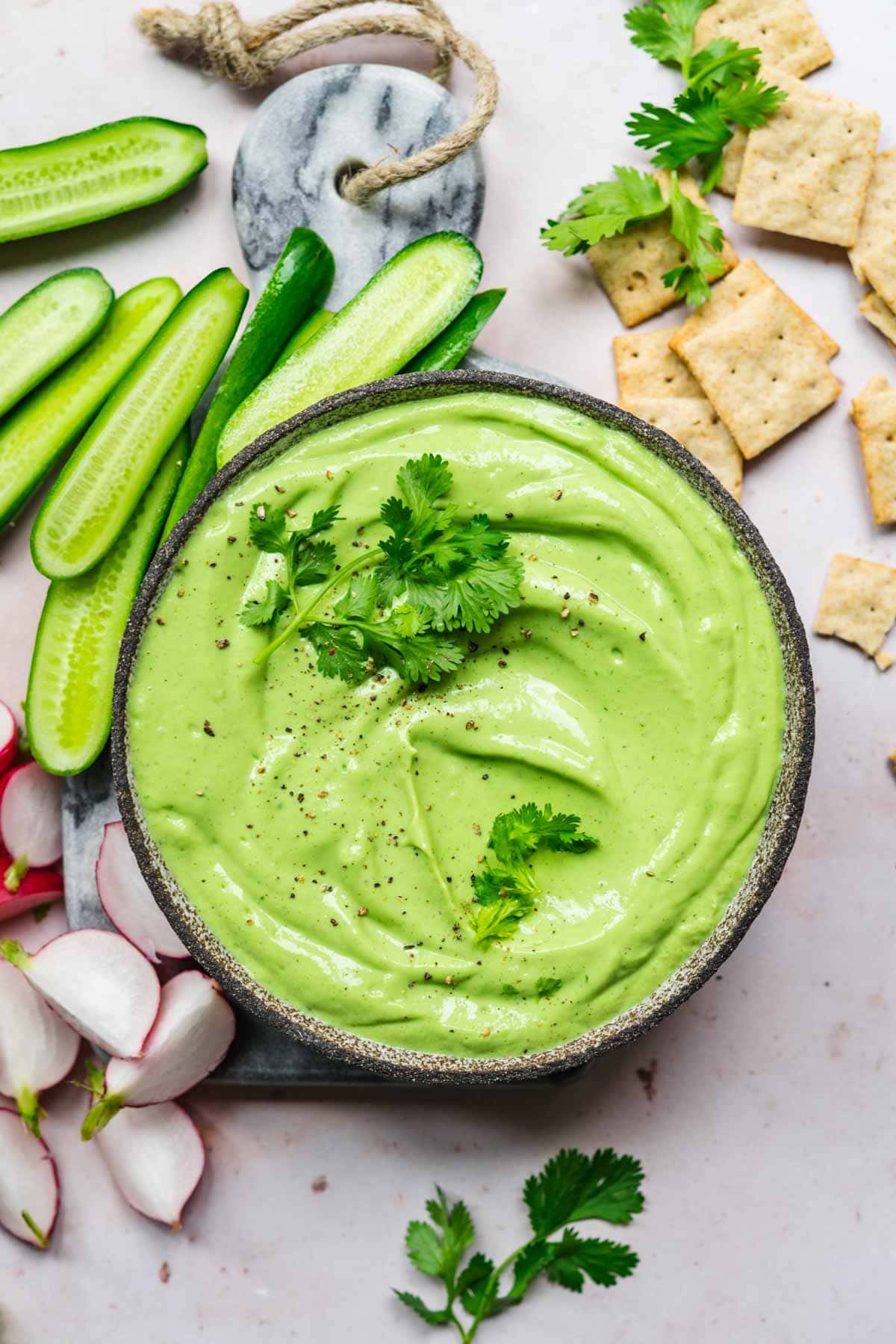 overhead view of herb tofu dip in bowl with fresh vegetables and crackers next to it. 