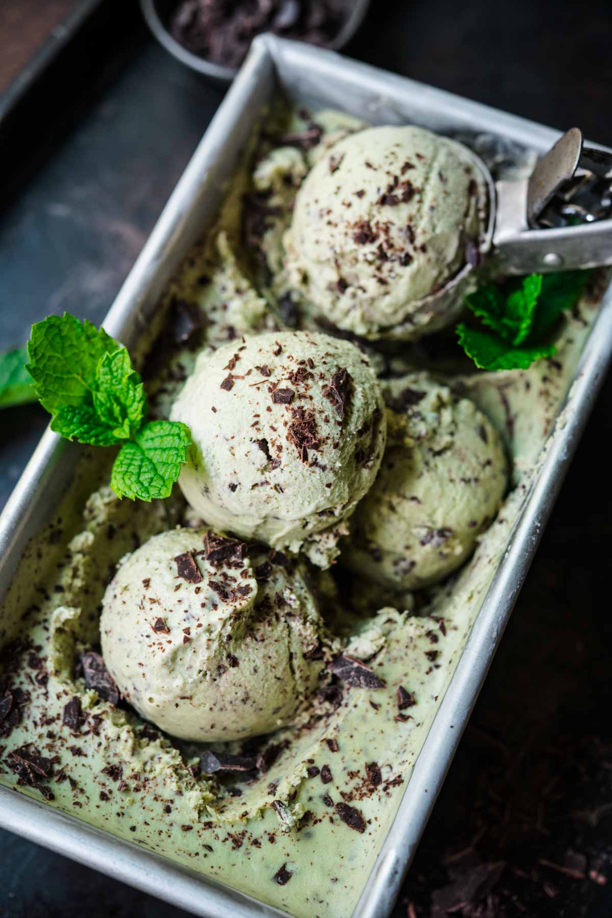 close up view of several scoops of vegan mint chocolate chip ice cream in metal tin. 